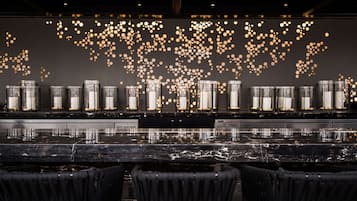 Una zona de bar con encimera de mármol reflectante, varias lámparas tipo vela y sillas tapizadas en negro.
