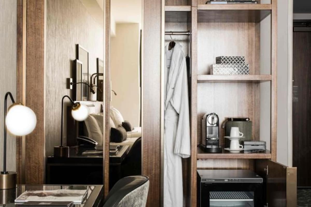 A hotel room with a wooden wardrobe, a desk with a lamp, a bed, and a shower area.