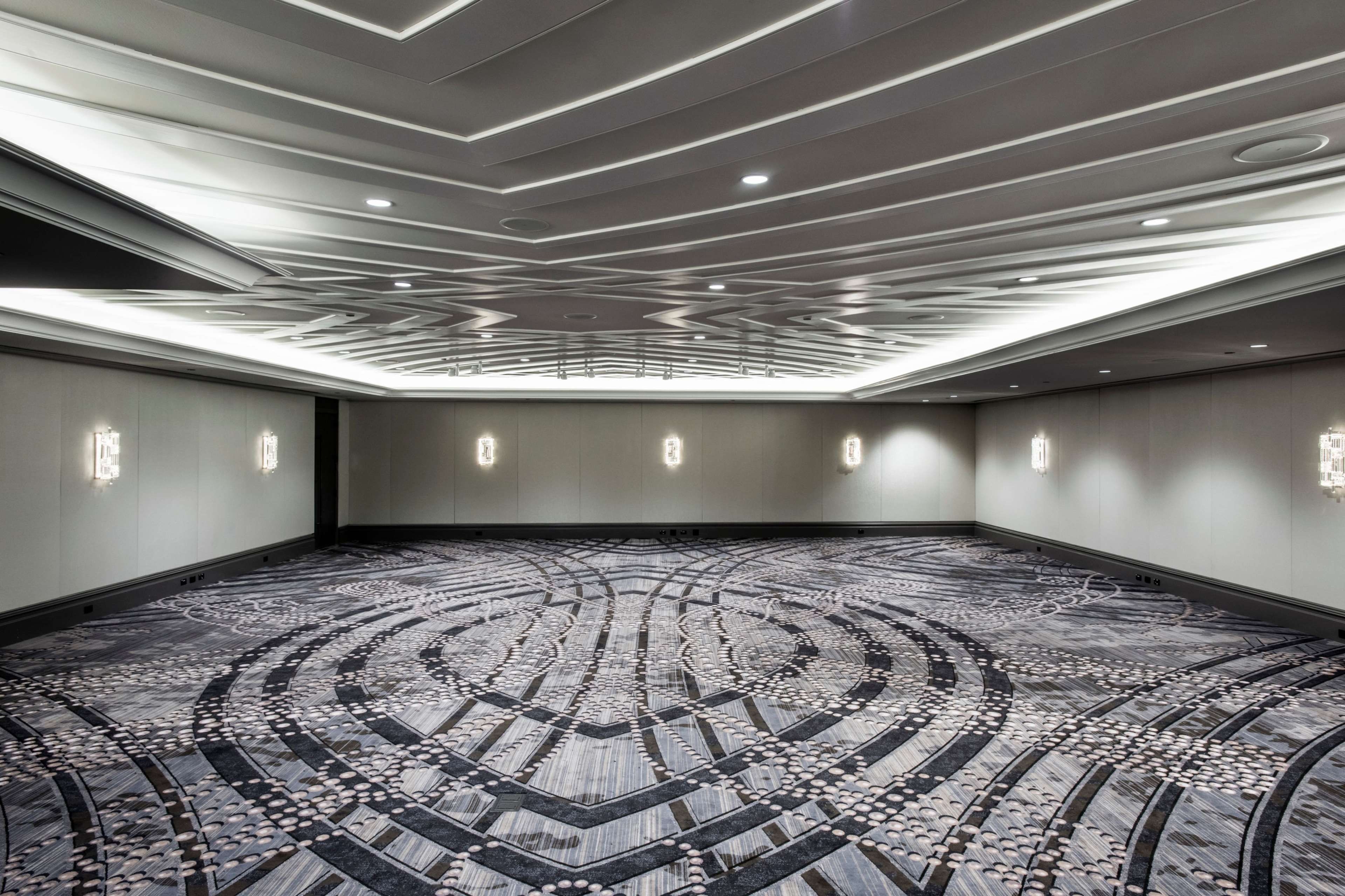 Una amplia sala de conferencias con alfombra estampada, iluminación empotrada en el techo y apliques de pared.