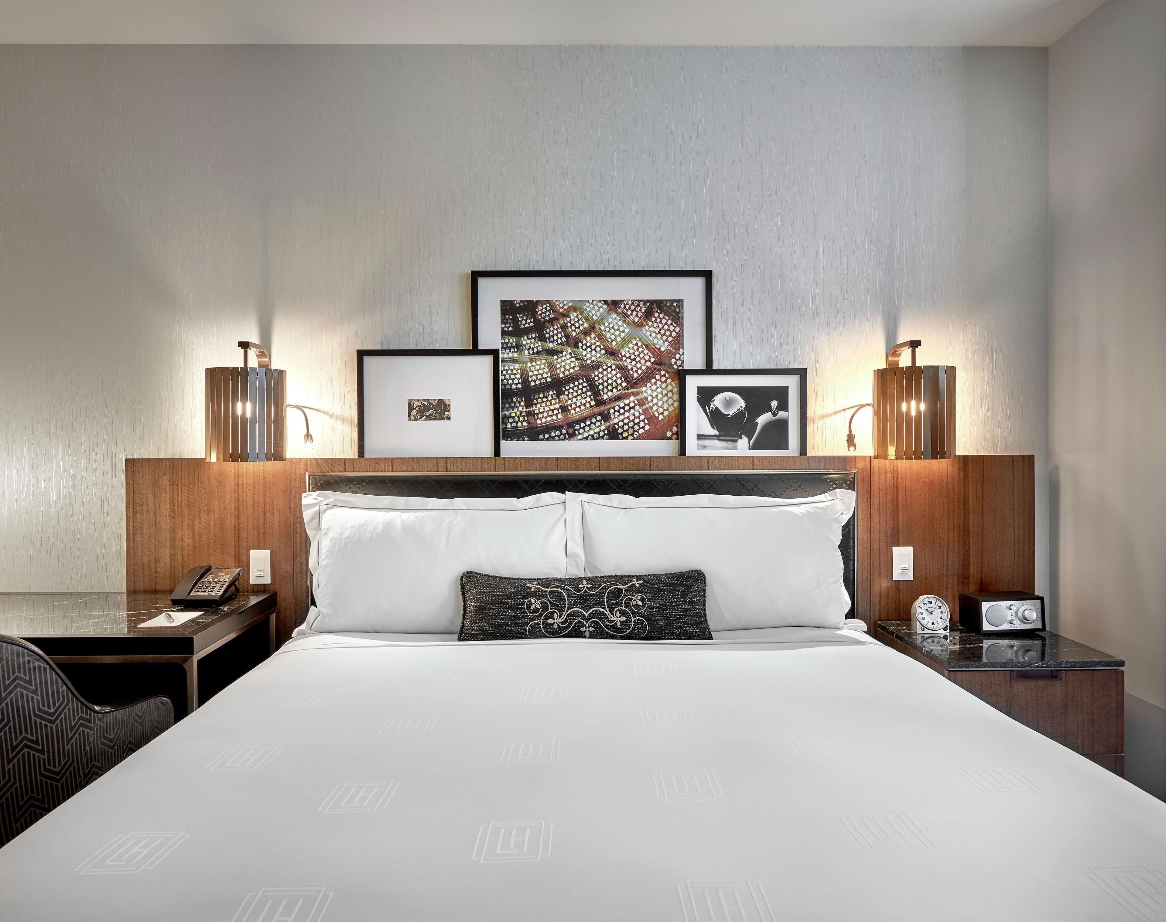 A hotel room with a bed, bedside tables, a telephone, a clock, and framed artwork on the wall.