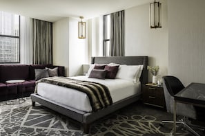 A modern hotel room with a large bed, a desk, a sofa, and a view of the city.