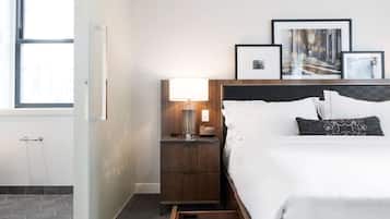 Una habitación de hotel con cama, mesita de noche con lámpara, cajón de madera y cuadros en la pared.
