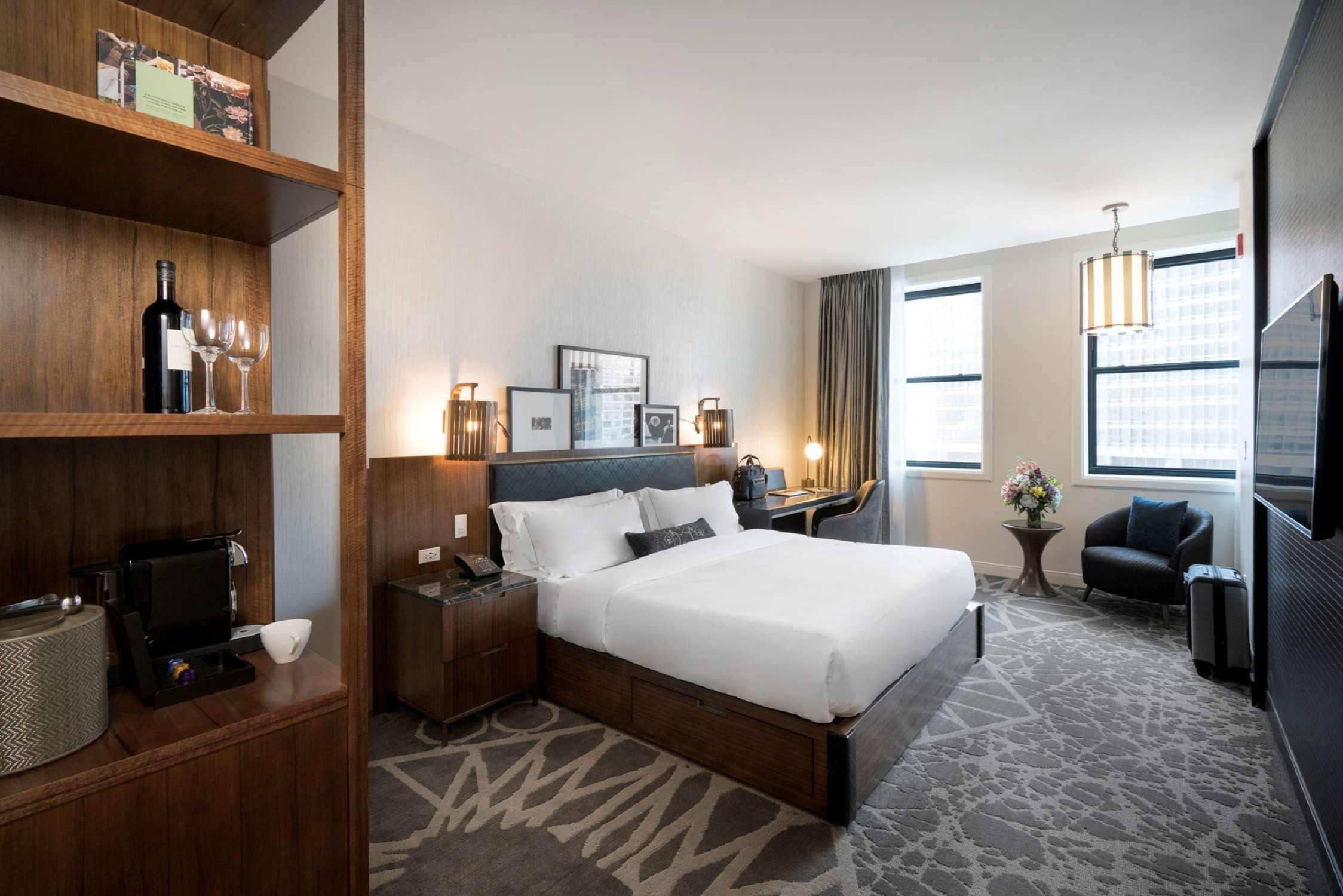 Ein Hotelzimmer mit Bett, Nachttisch, Lampe, Schreibtisch, Stuhl und Fernseher.