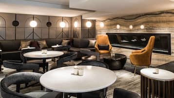 A modern lounge area with sofas, round tables, and a fireplace.