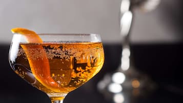 Un vaso de cóctel con un adorno cítrico sobre una superficie reflectante.