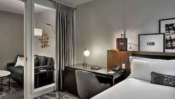 Quarto de hotel com cama, escrivaninha, cadeira e um pequeno espaço de estar com sofá.