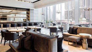 A modern interior with seating areas, a bar, and large windows offering a city view. - LondonHouse Chicago, Curio Collection by Hilton (Chicago)