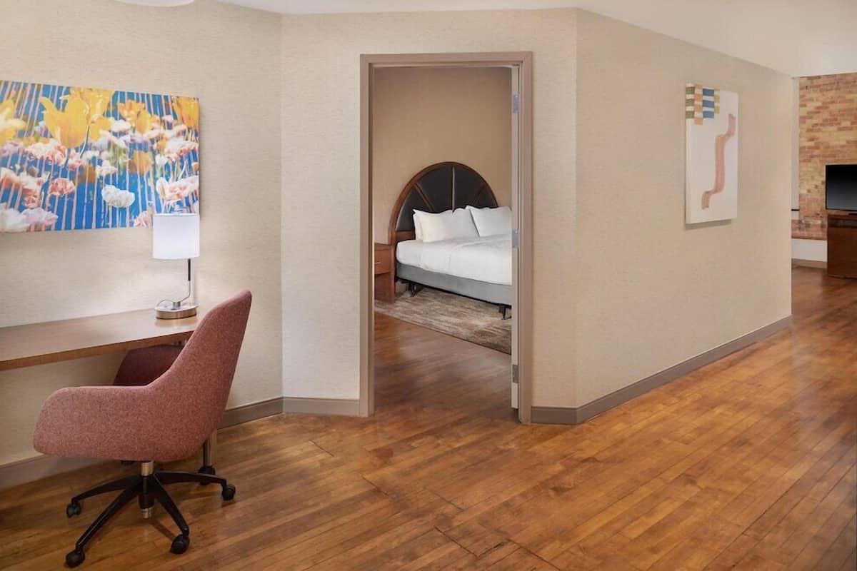 A hotel room with a desk, chair, bed, and artwork on the walls.