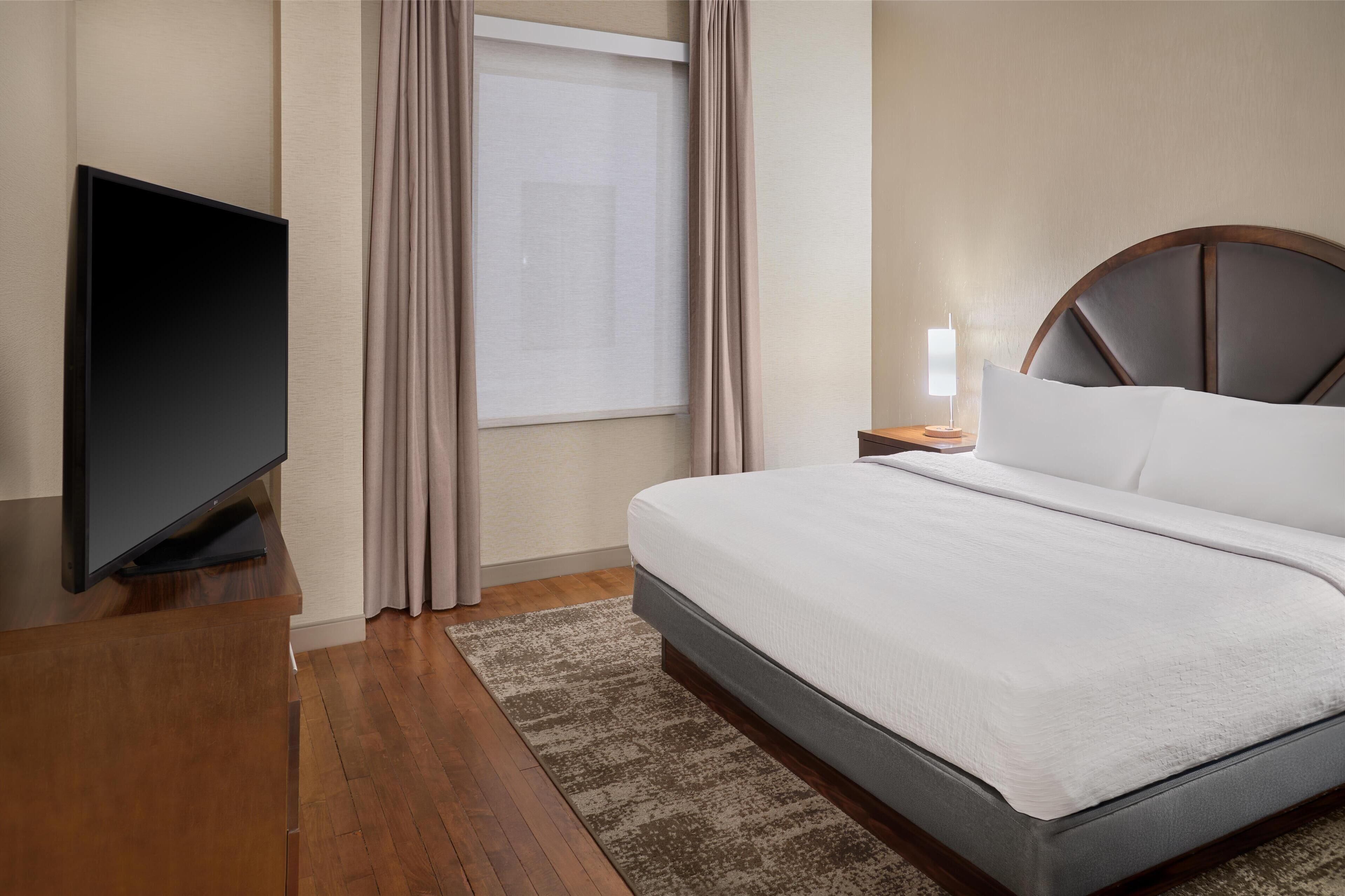 A hotel room with a bed, a TV, a nightstand, and a window with curtains.