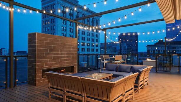 Una terraza al aire libre con chimenea, asientos e iluminación colgante frente a un horizonte urbano.