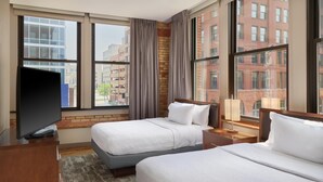 Habitación de hotel con dos camas, televisión y ventanas amplias con vistas a la ciudad.