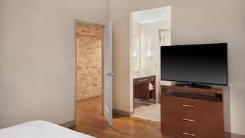 Un dormitorio con pared de ladrillo, cómoda de madera, televisor de pantalla plana y cama.