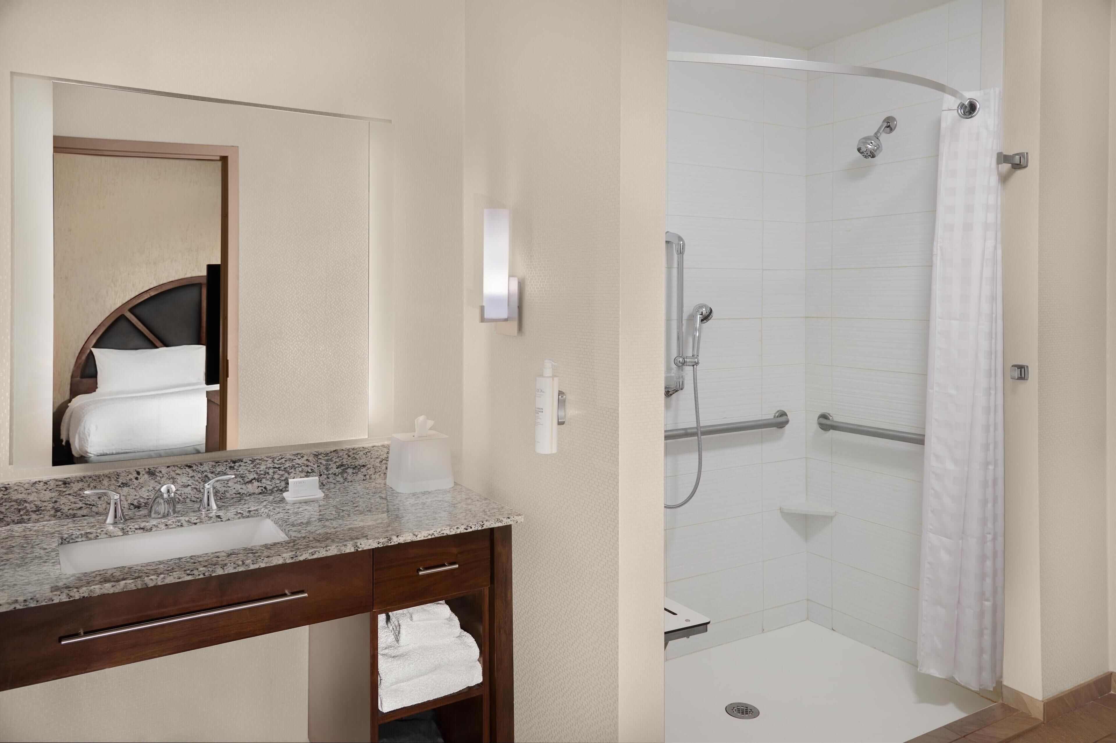 A bathroom with a granite countertop sink, a mirror, a towel rack, and a walk-in shower with a glass door.