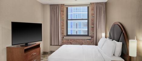 A hotel room with a flat-screen TV, a bed with white linens, a wooden nightstand, and a ceiling fan.