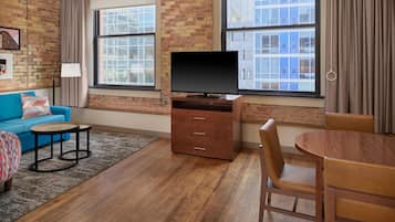 Een moderne woonkamer met een blauwe bank, een houten salontafel, een tv op een houten kast, en een eettafel met stoelen.