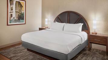 Una cama bien tendida con cabecera de madera, dos mesitas de noche con lámparas y un cuadro en la pared.