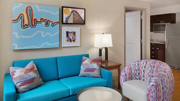 Een woonkamer met een blauwe bank, een gestreept fauteuil, een kleine tafel en een lamp. Twee kunstwerken hangen in lijsten aan de muur.