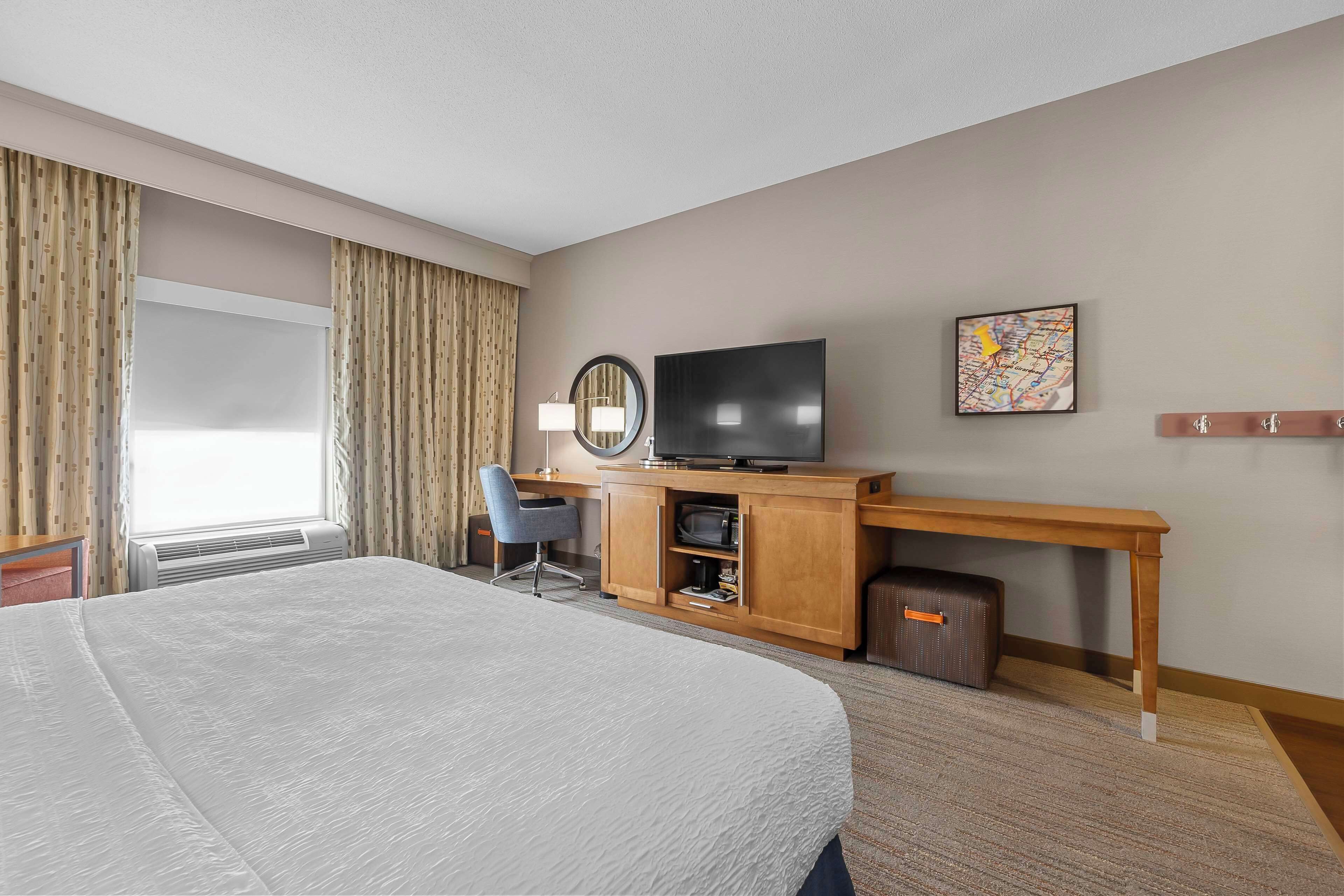 A hotel room with a large bed, a desk with a television, a chair, and a map on the wall.