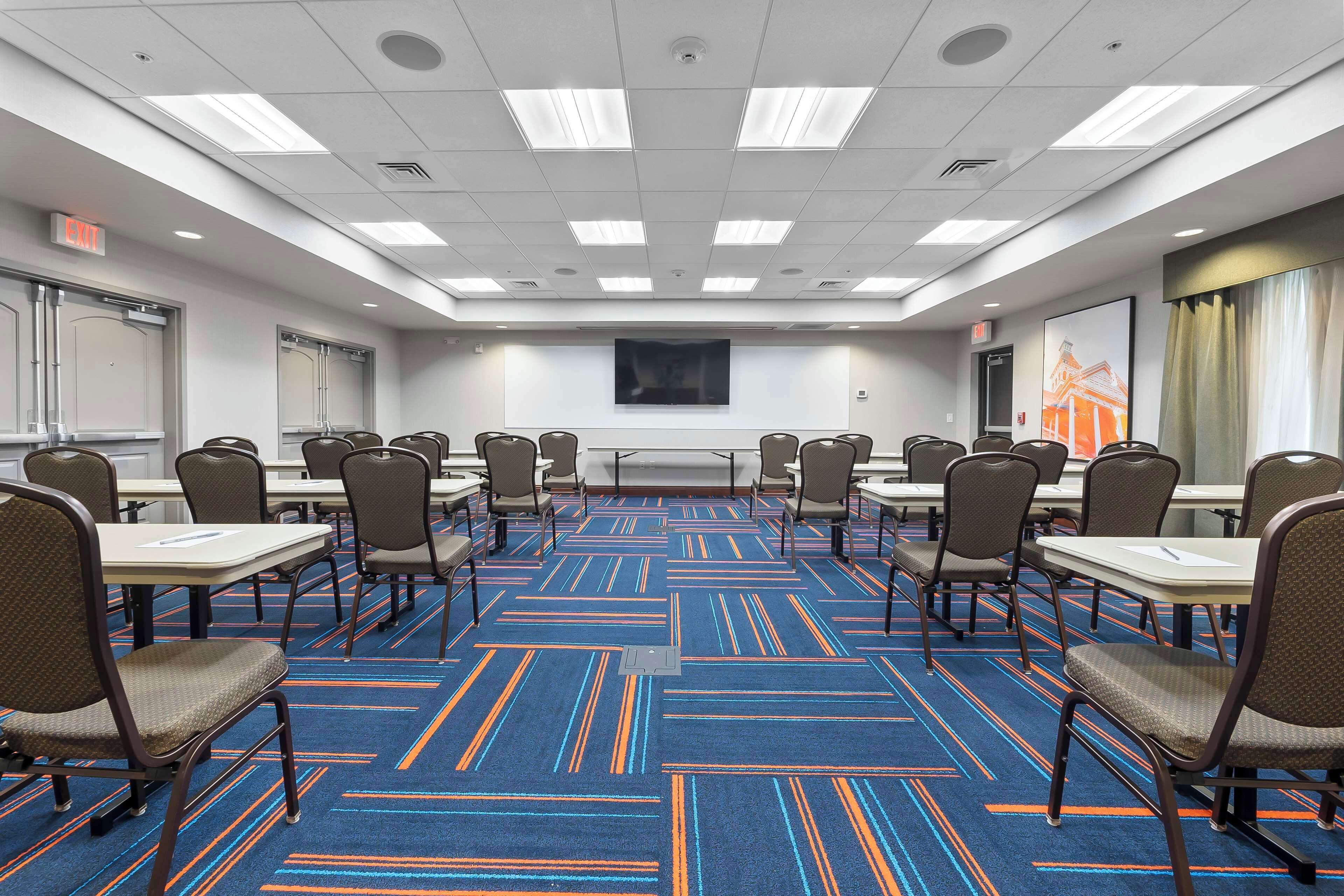 Una sala de conferencias con alfombra azul, paredes blancas y una pantalla grande.