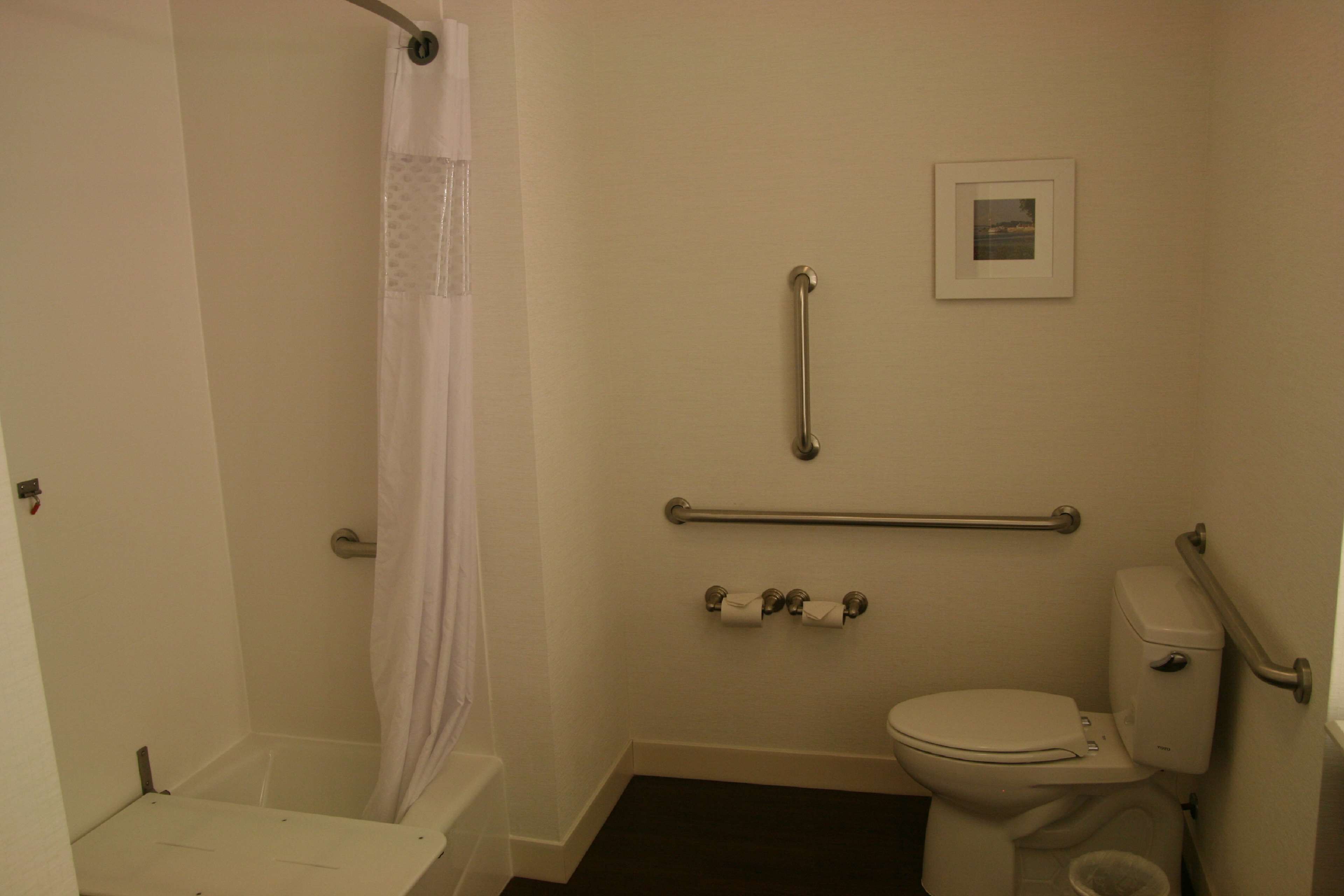 A small, basic bathroom with a toilet, a shower, and a grab bar.