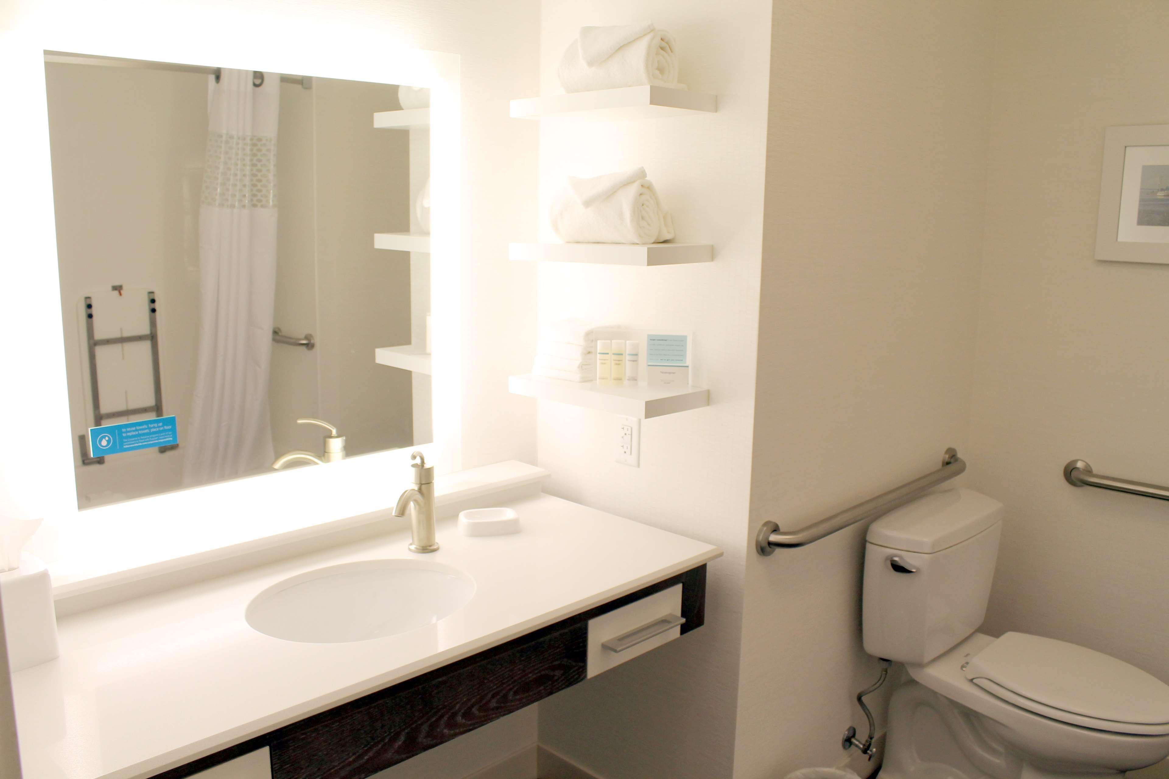 A bathroom with a white sink, mirror, and toilet. There are shelves above the sink holding toiletries.