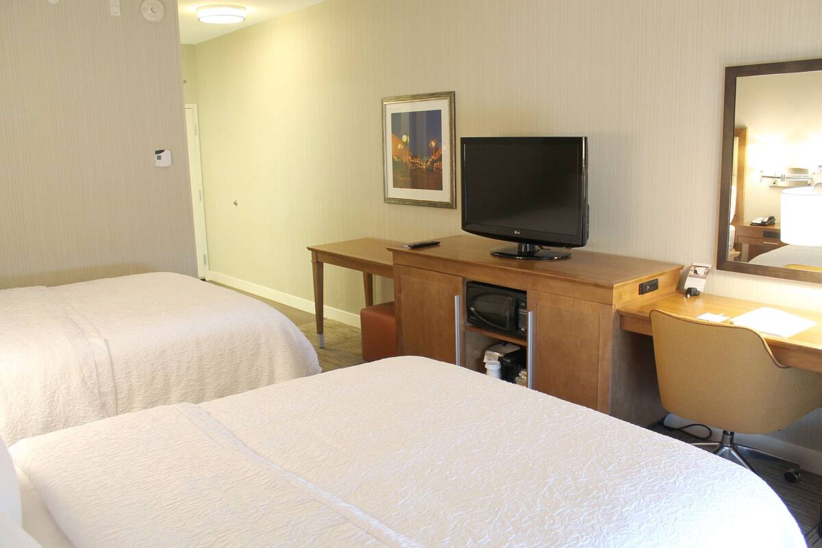 A hotel room with two beds, a desk with a television, a microwave, and a mirror.