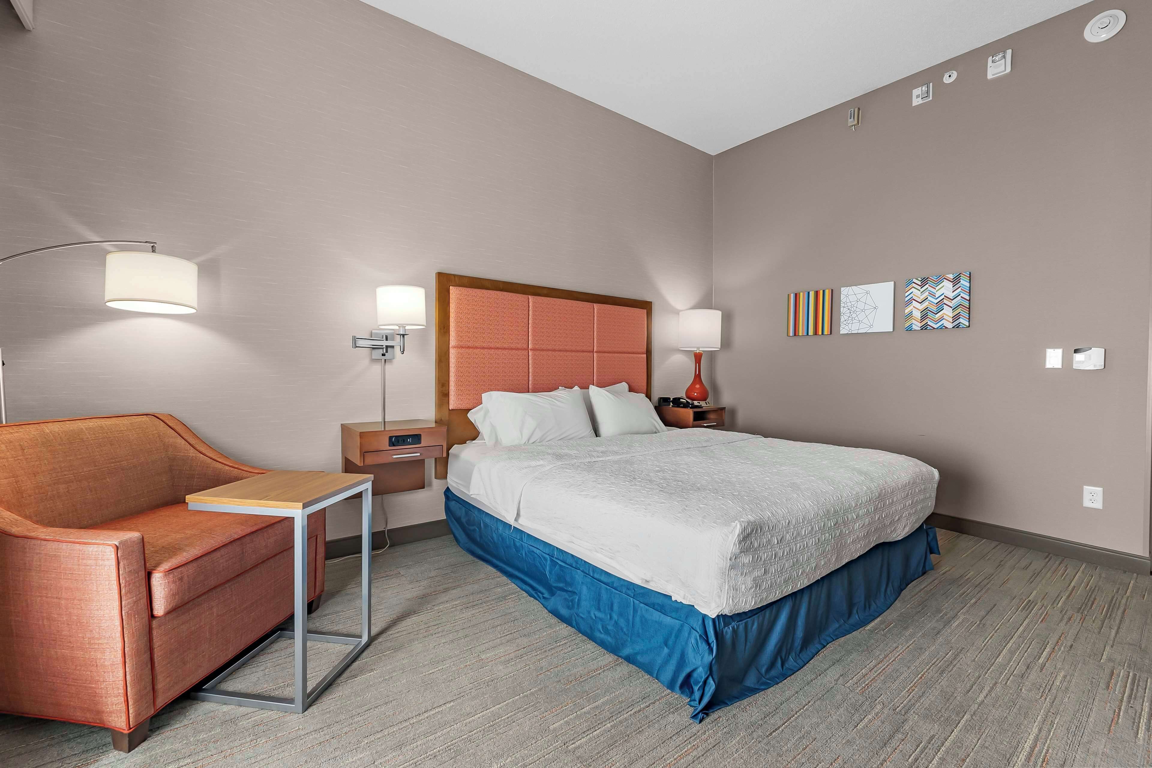 Una habitación de hotel con cama, sofá, mesita de noche, lámpara y decoración en la pared.