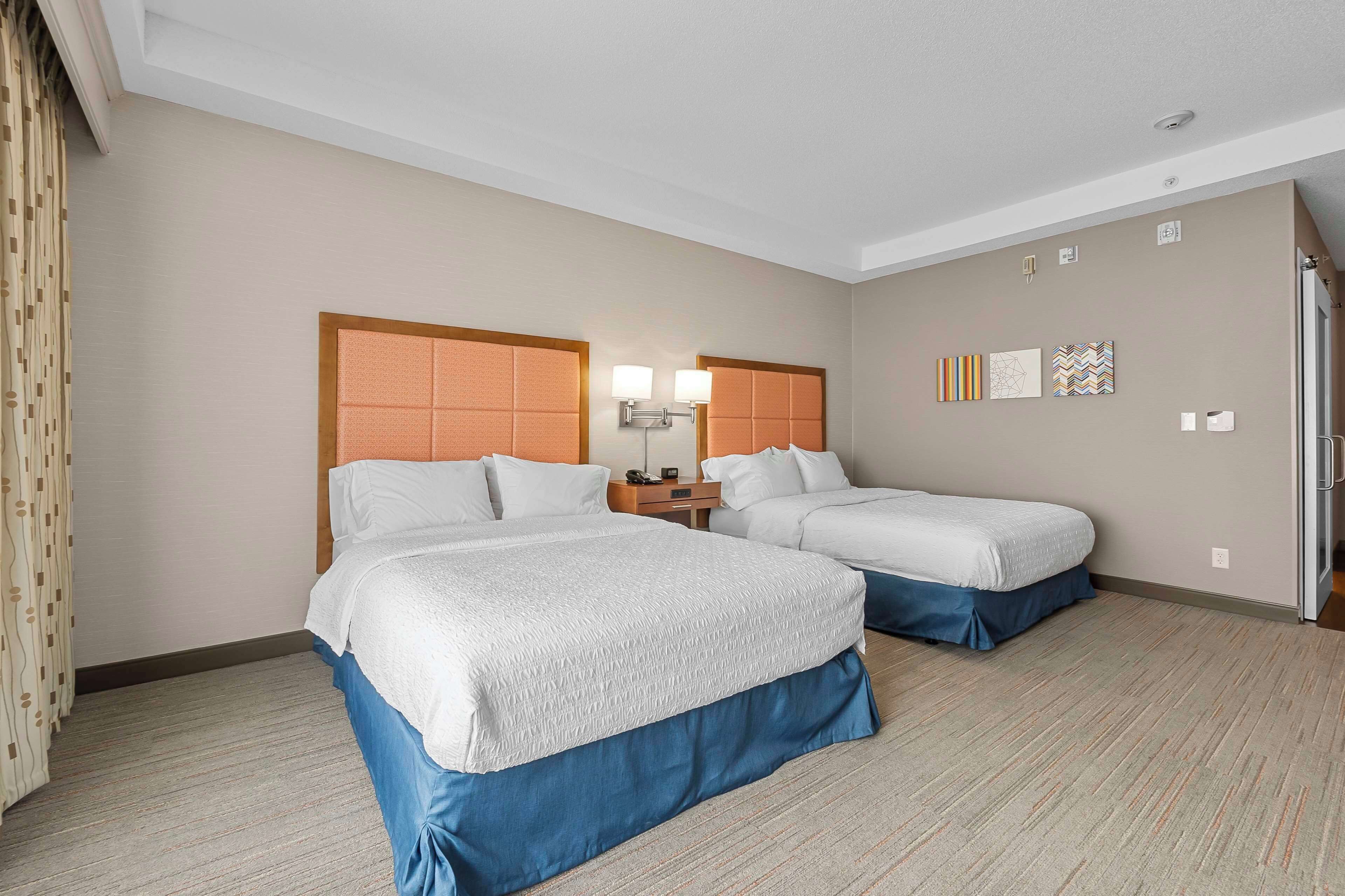 A hotel room with two beds, a nightstand, and a wall with artwork.