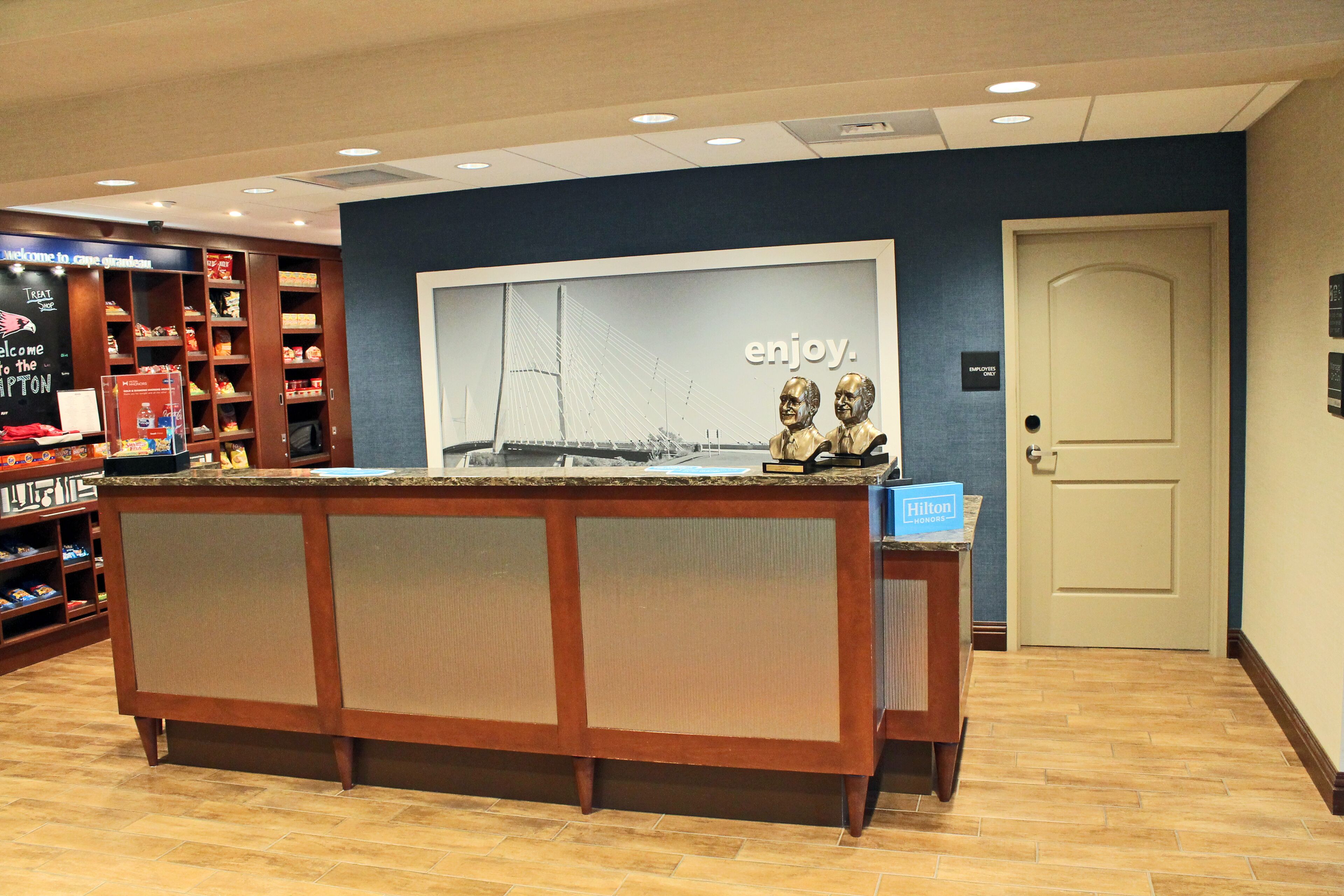 A reception desk with a large window displaying a bridge, a sign reading "enjoy.", and a "Hilton" sign on the counter.