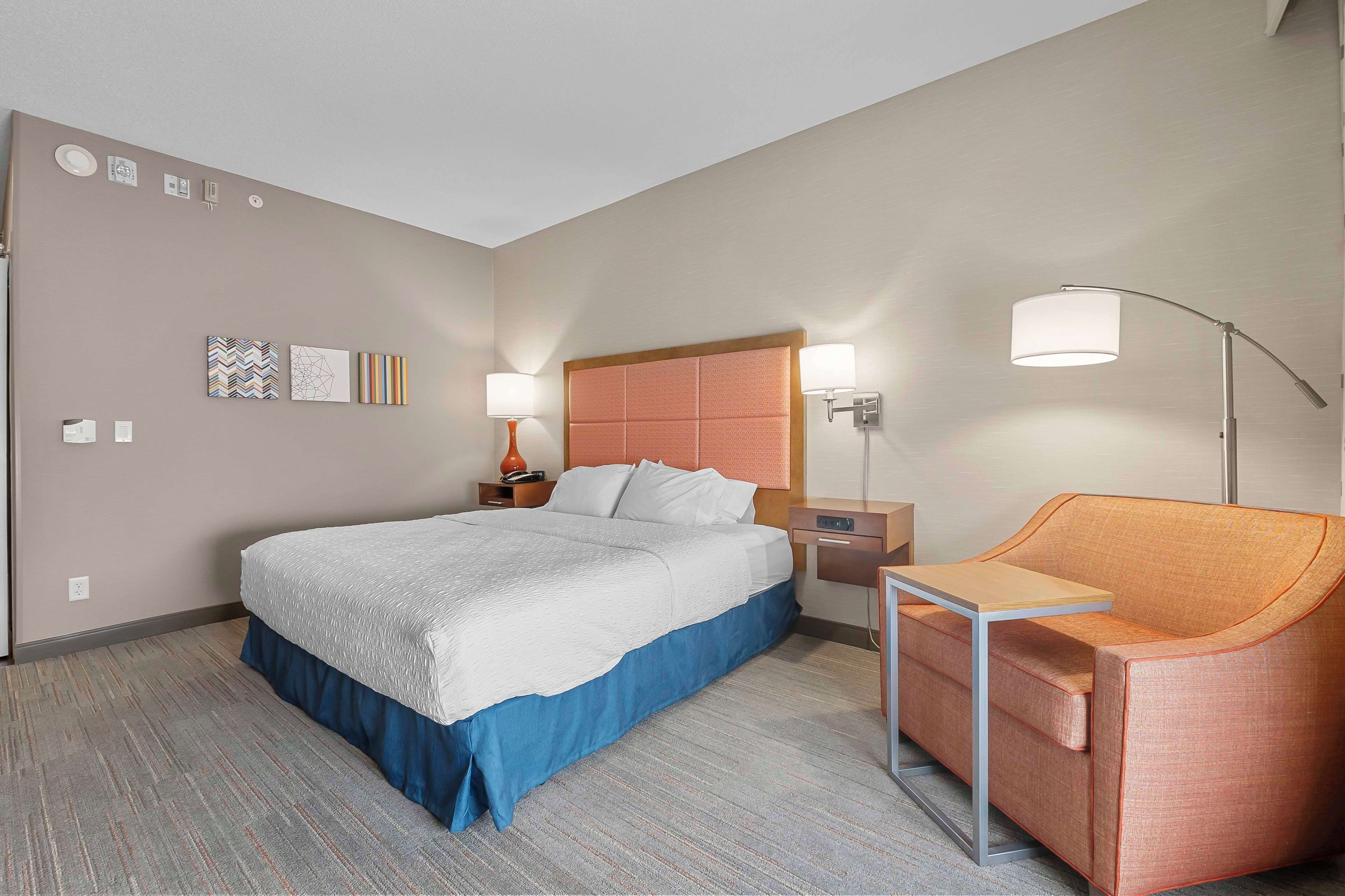 Habitación de hotel con cama, escritorio, silla, mesita de noche, lámpara y decoración en la pared.