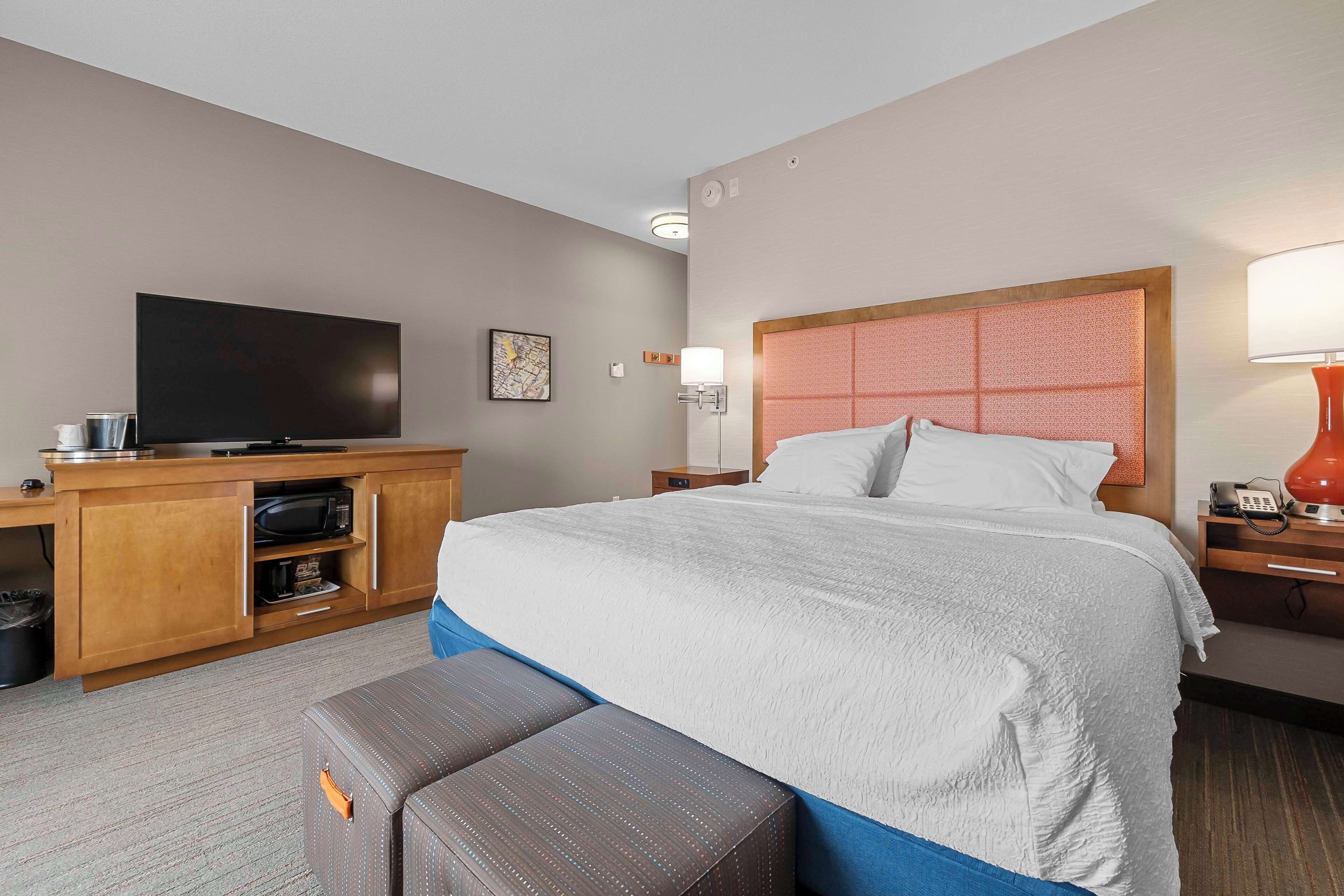 Et hotelværelse med en stor seng, et fjernsyn, et skrivebord med mikroovn og en rød lampe.