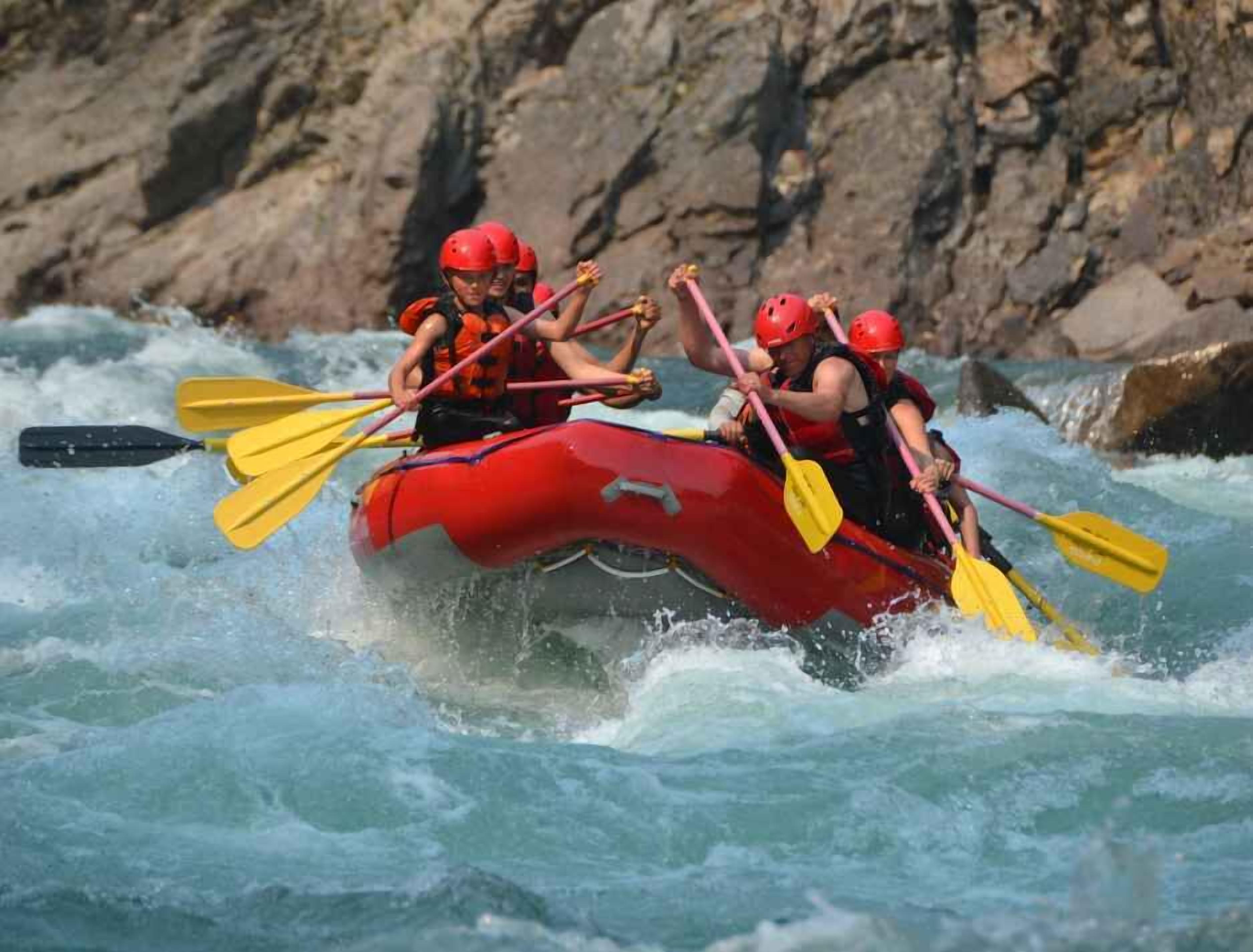 A group of people in a red raft navigating a river with rapids.