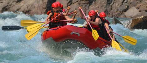 A group of people in a red raft navigating a river with rapids.