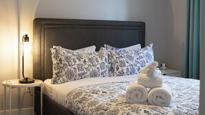 Ein ordentlich gemachtes Bett mit einem gemusterten Überwurf, einer Nachttischlampe und einem Deckenventilator.
