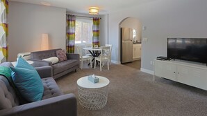 Ein Wohnzimmer mit Sofa, Couchtisch, Fernseher und einem Essbereich mit Stühlen und Tisch.
