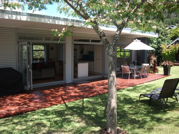 A house with a patio area, a dining table with chairs, and a barbecue grill. - Waimarie Villa (Hahei)