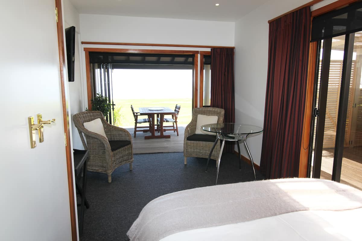 A hotel room with a bed, two wicker chairs, a small glass table, and a view of the outdoors.