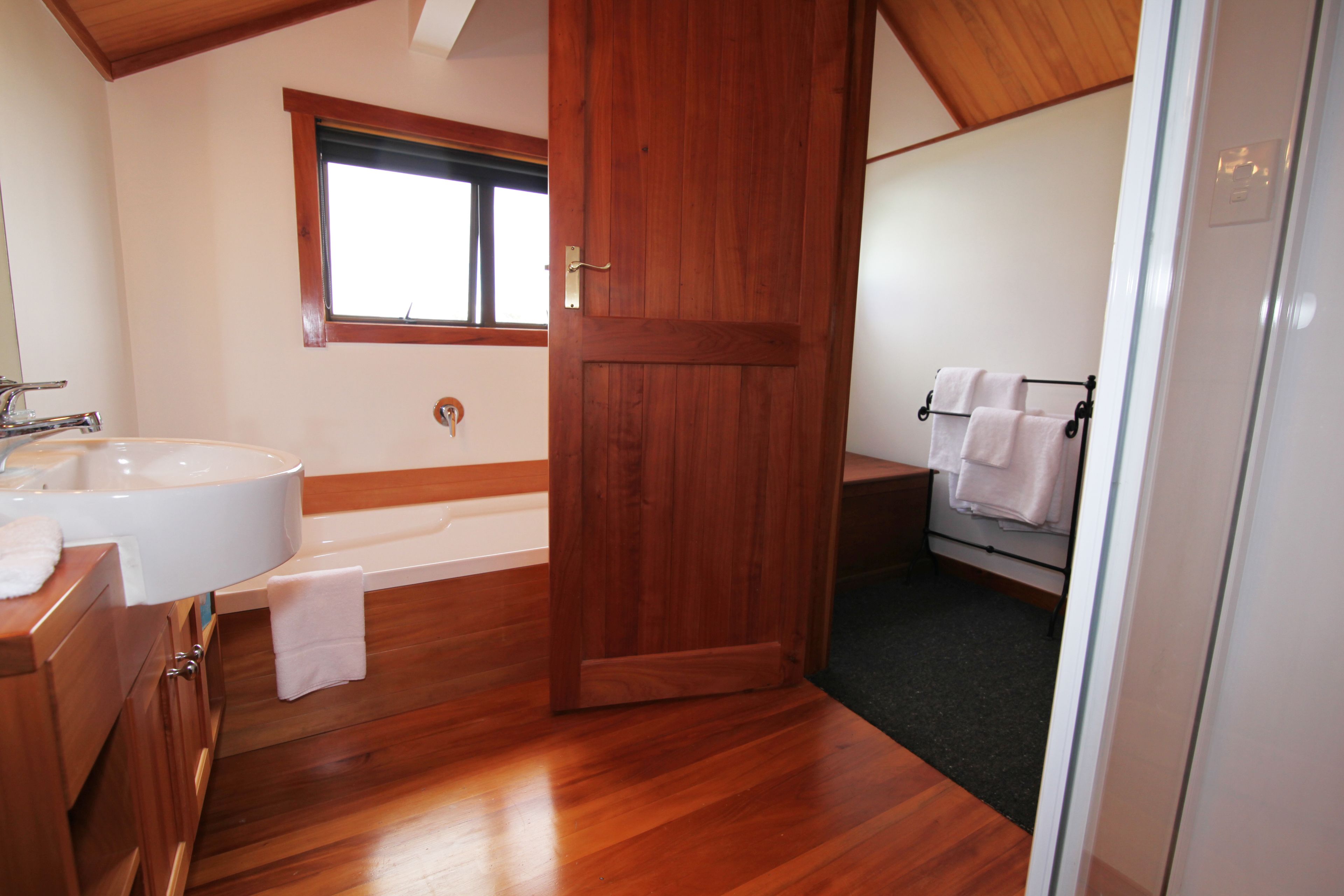 A bathroom with a wooden floor, a bathtub, a sink, and a window.