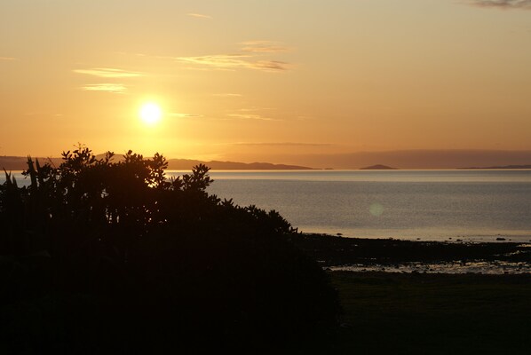 A sunset over a calm sea with distant landforms. - Te Puru Beach Lodge (Te Puru)