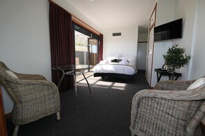 A hotel room with a bed, two wicker chairs, a glass table, a TV, and a plant. - Te Puru Beach Lodge (Te Puru)