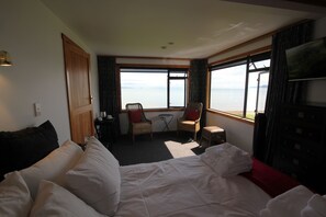 A hotel room with a large bed, two chairs, a small table, and a view of the sea. - Te Puru Beach Lodge (Te Puru)