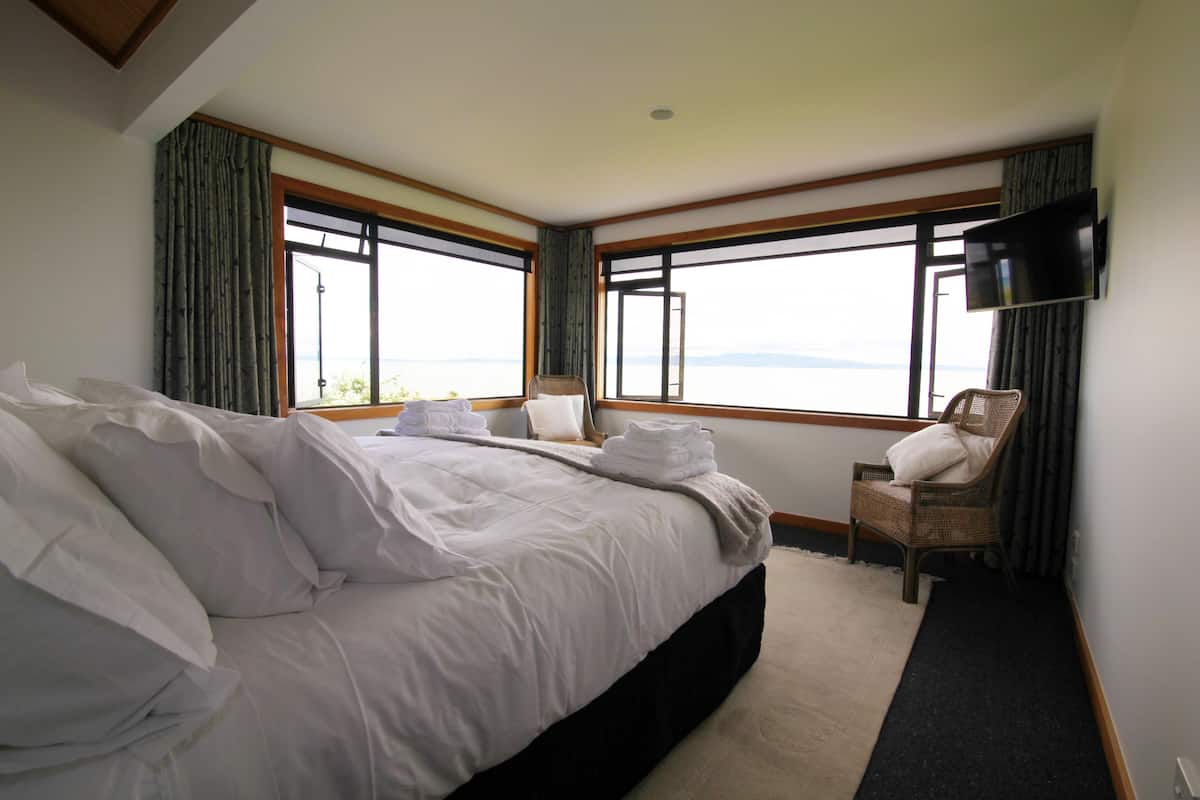 A hotel room with a large bed, a chair, a television, and a view of the sea.