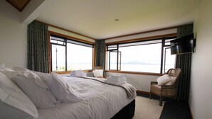 Ein Hotelzimmer mit einem großen Bett, einem Sessel, einem Fernseher und Blick auf das Meer.