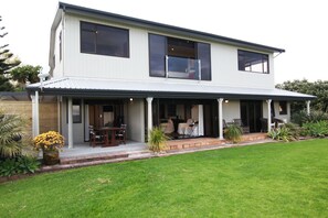 A two-story house with a covered porch, a lawn, and potted plants. - Te Puru Beach Lodge (Te Puru)