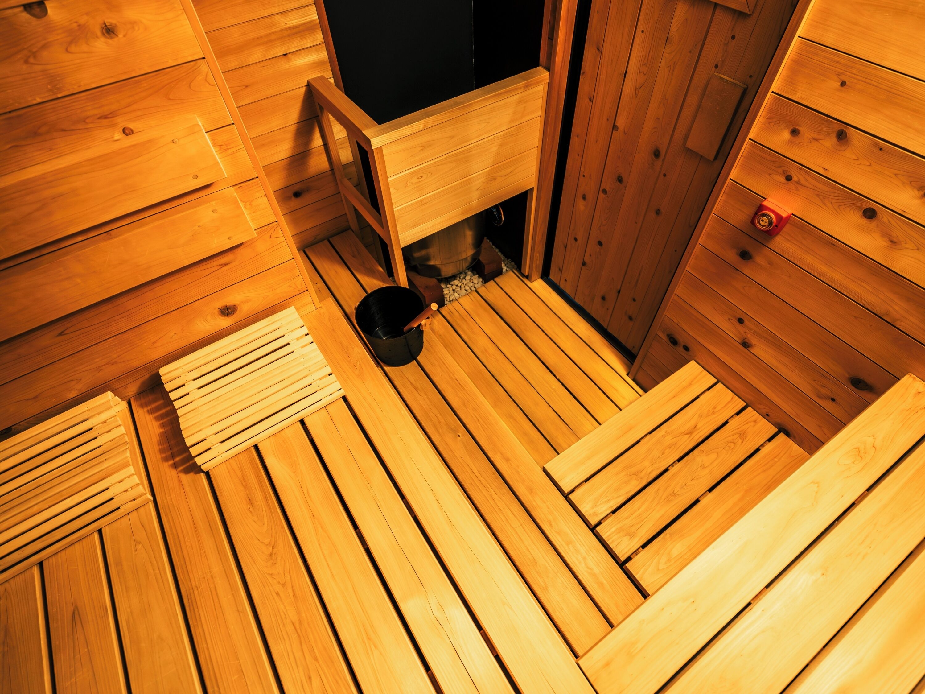 A sauna room with wooden floors, a black heater, and a wooden bench.