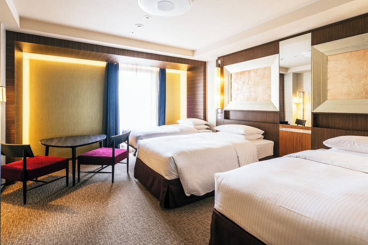 Habitación de hotel con dos camas, un escritorio, una silla y un espejo grande.