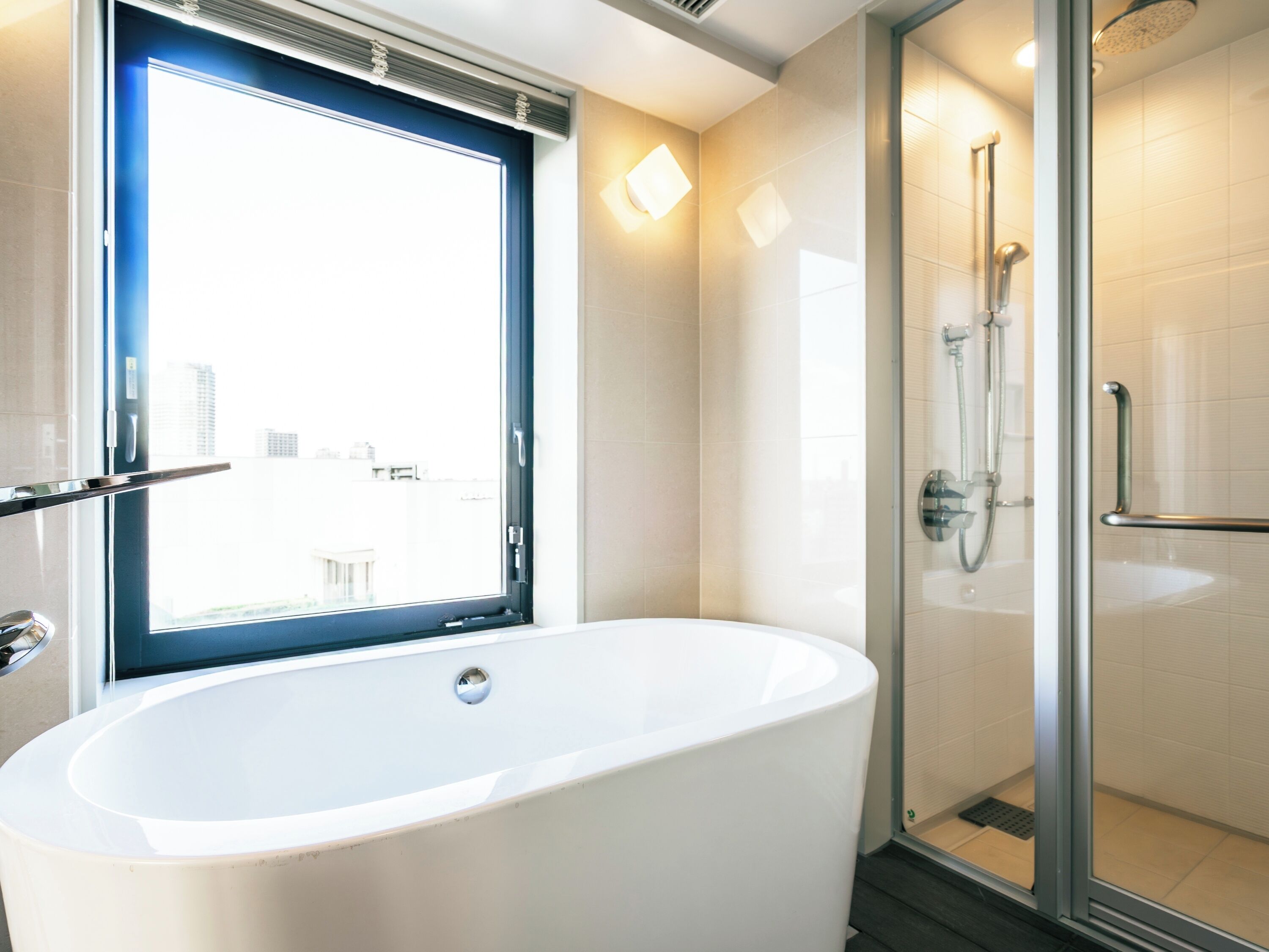 Een moderne badkamer met een vrijstaand bad, een douchecabine met glazen wanden en een raam met uitzicht op de stad.