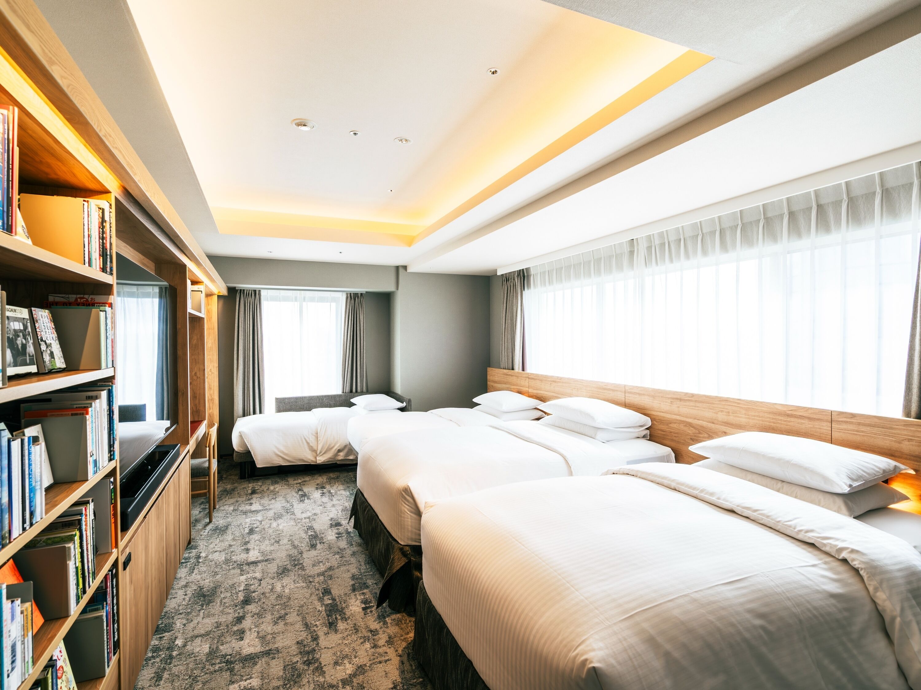A hotel room with a large bed, a bookshelf, and a window with curtains.