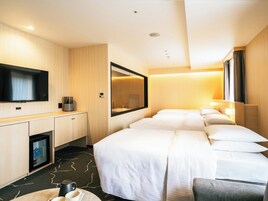 A hotel room with a TV, a mini-fridge, a desk, and a bed with multiple pillows.