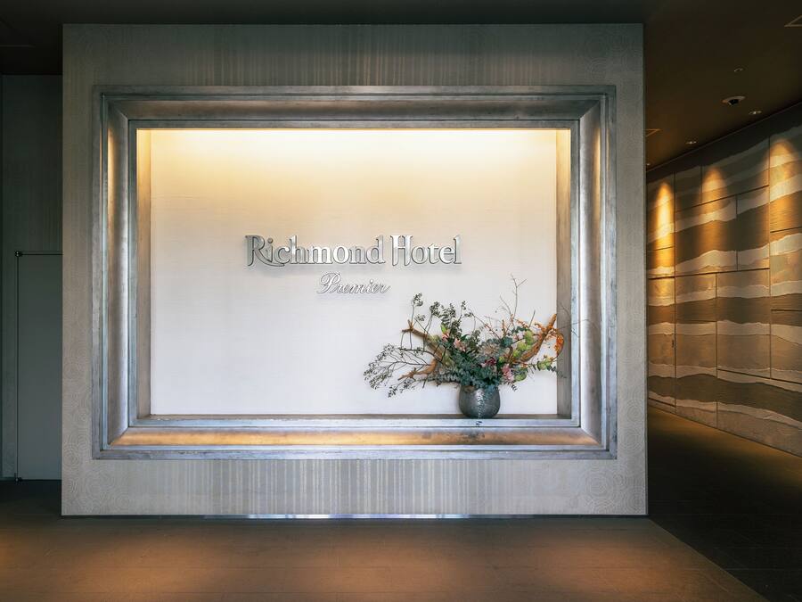 Un área de recepción con un cartel enmarcado que dice 'Richmond Hotel Premier' y un jarrón con flores.